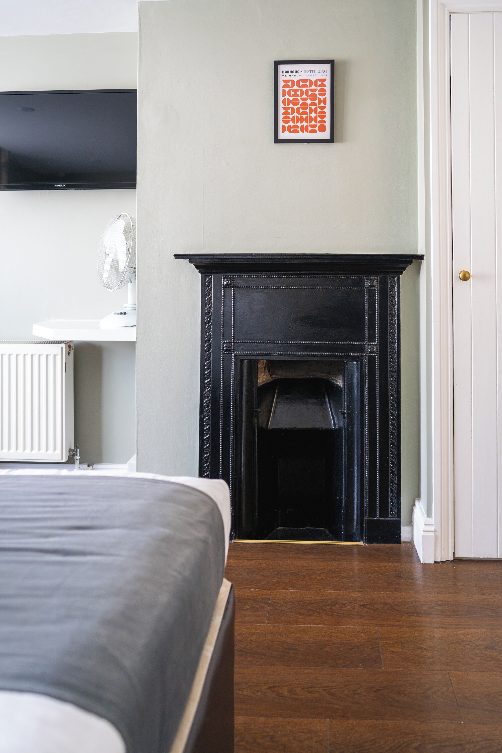A bedroom with a bed, a fireplace, a radiator, and a framed picture on the wall.