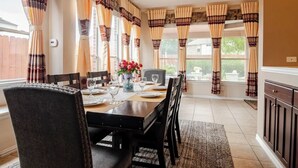 Een eetgedeelte met een lange tafel voor vier personen, omlijst door gordijnen met een patroon.