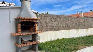 An outdoor brick oven barbecue grill attached to a white wall, with a grassy area in front and a wooden fence in the background. - SAONA VILLAS (VN VERDA): villa for 6 people, private pool, wifi, air co (Les Tres Cales)