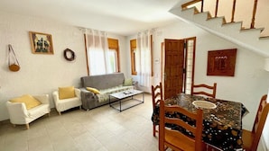 A living room with a sofa, chairs, a dining table with chairs, a staircase, and a door. - SAONA VILLAS (VN VERDA): villa for 6 people, private pool, wifi, air co (Les Tres Cales)