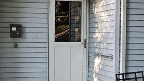 A white door with a glass panel, a mailbox, and a metal gate on a house with horizontal siding. - Indian Lake House (Worcester)