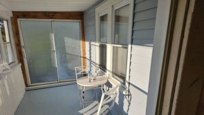 A small outdoor patio with a white table and chairs, a sliding glass door, and a sign indicating a smoking area. - Indian Lake House (Worcester)