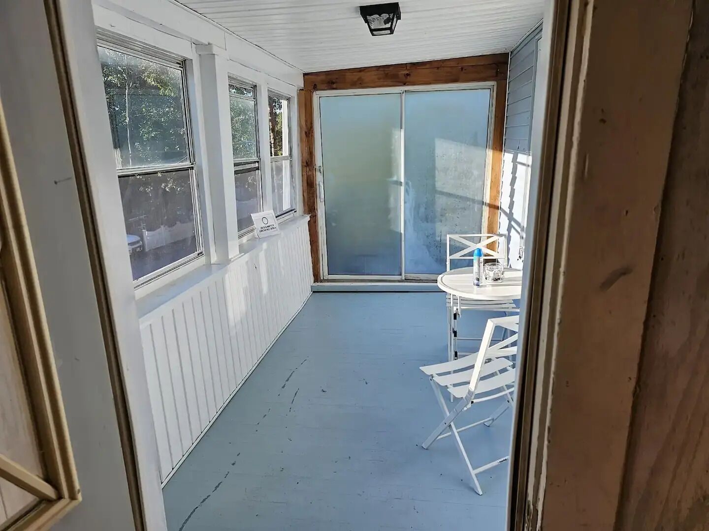 A narrow balcony with a table and chairs, a sliding glass door, and a view of the outside.