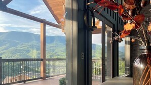 Ein Balkon mit Blick auf eine gebirgige Landschaft, eine Vase mit getrockneten Ästen und ein hölzernes Geländer.