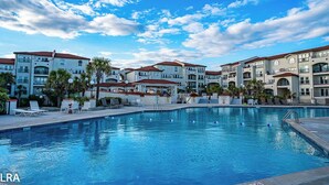 Una piscina con sillas de descanso y un pabellón, rodeada de edificios de varios pisos con balcones y palmeras.