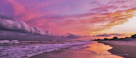 A beach with a sunset, waves, and distant houses.