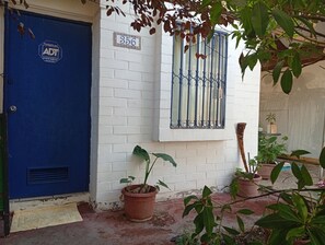 A blue door with a number plate, a white brick wall, a window with metal bars, and potted plants.