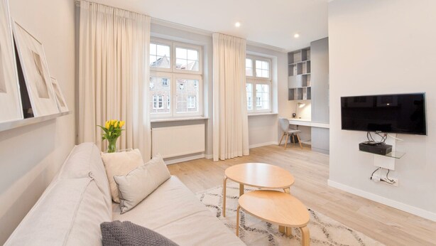 A modern living room with a sofa, two small tables, a TV, and a window with curtains. - Apartament Lili by Q4Apartments  (Gdansk)
