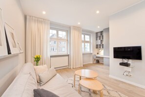 A modern living room with a sofa, two small tables, a TV, and a window with curtains. - Apartament Lili by Q4Apartments  (Gdansk)