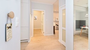 A modern kitchen with white cabinets, a wooden floor, and a dining area with a grey cushioned bench. - Apartament Lili by Q4Apartments  (Gdansk)