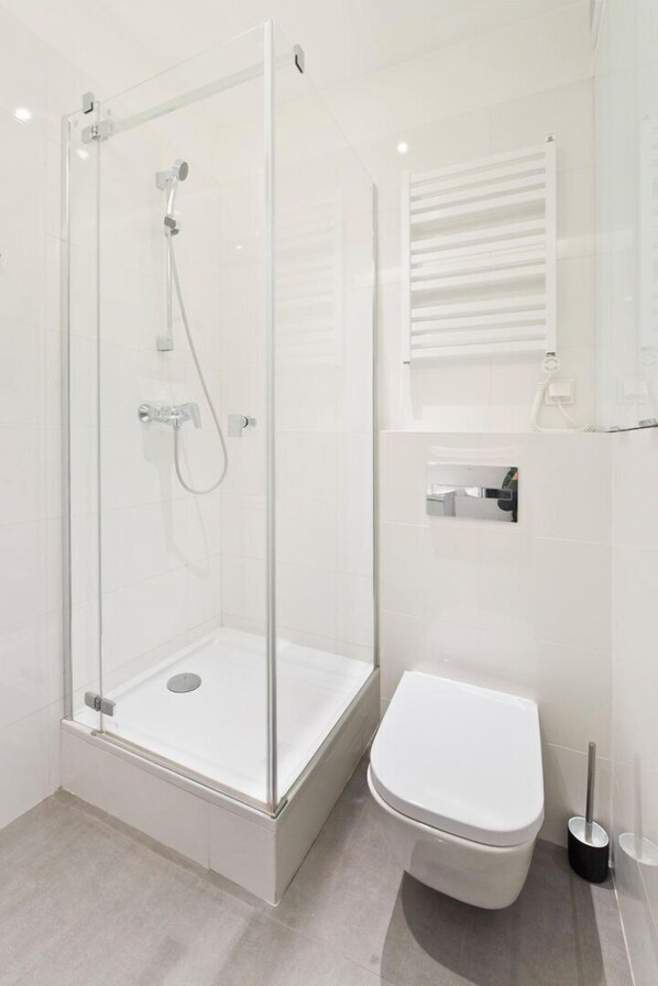 A modern bathroom with a glass-enclosed shower, a white toilet, and a small window with a towel rack. - Apartament Lili by Q4Apartments  (Gdansk)