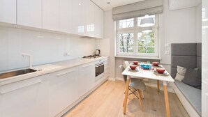 A modern kitchen with white cabinets, a dining table with red and blue bowls, and a grey sofa. - Apartament Lili by Q4Apartments  (Gdansk)