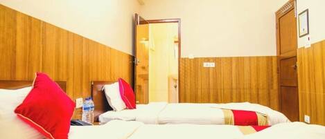Habitación de hotel con dos camas, paneles de madera en las paredes, una puerta y una mesita con una botella de agua.