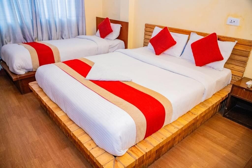A hotel room with two beds, each with white bedding and red accents, wooden headboards, and a wooden floor.