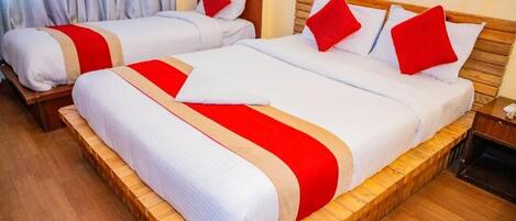 A hotel room with two beds, each with white bedding and red accents, wooden headboards, and a wooden floor.