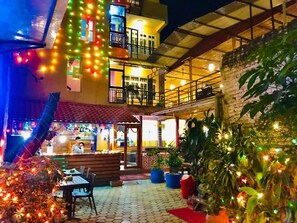 An outdoor dining area with tables and chairs, surrounded by potted plants and illuminated by string lights. - Doors Hotel (Kathmandu)