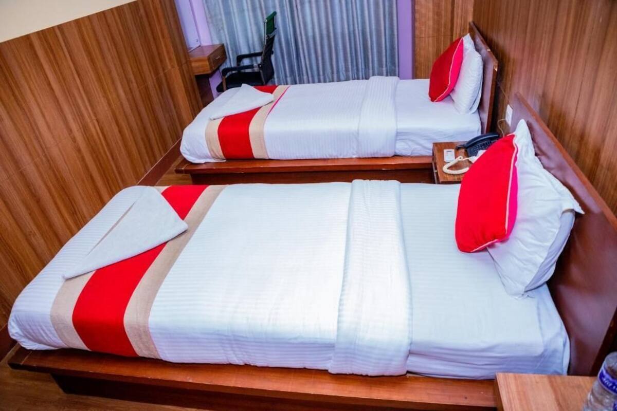 Two beds with white bedding and red accents, wooden headboards, and a small bedside table with a telephone.
