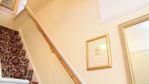 En trappa med ett mönstrat mattgolv, en inramad tavla på väggen och en spegel.