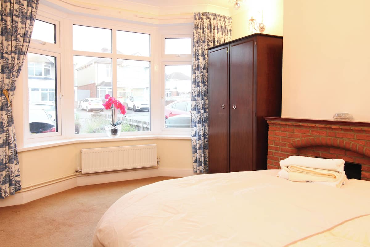 A bedroom with a large bed, a fireplace, a wardrobe, and a window with curtains.