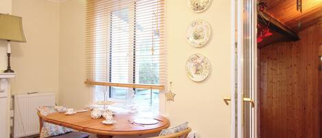 A dining area with a wooden table and chairs, a window with blinds, and three decorative plates on the wall.