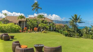 A well-maintained lawn with wicker furniture, palm trees, and a view of a building with a mountain backdrop.