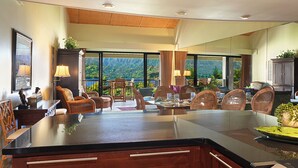 A spacious living area with a large island, dining table, and chairs. There are large windows offering a view of the mountains.