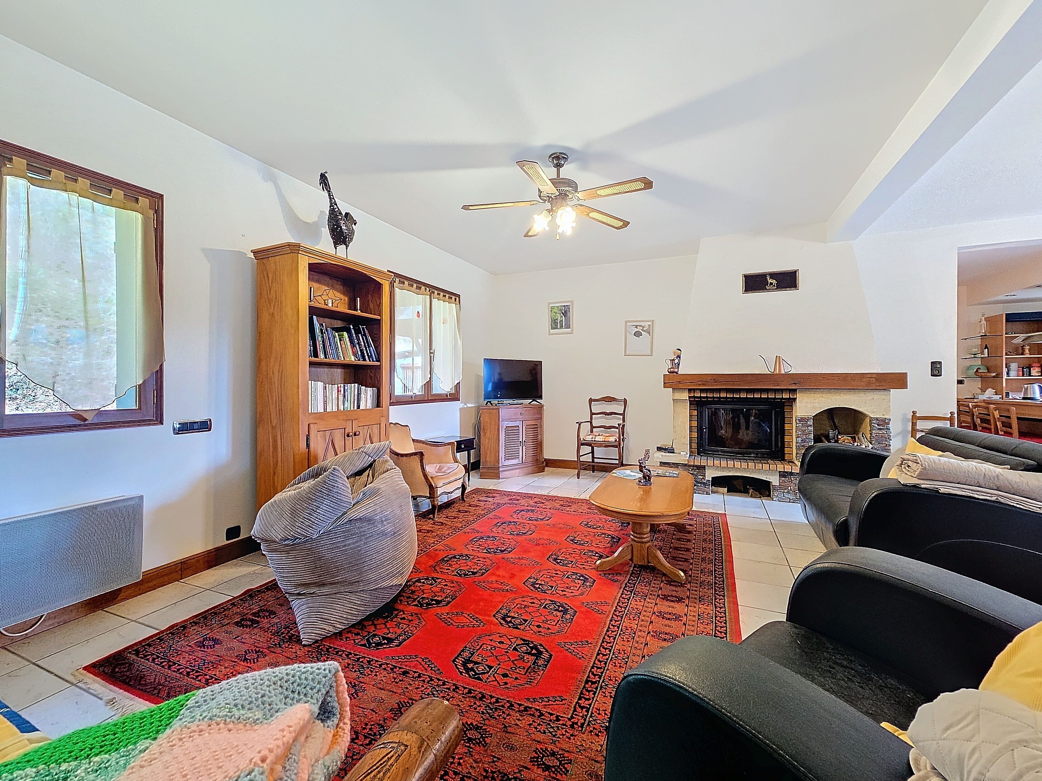 Ein Wohnzimmer mit Kamin, Bücherregal, Fernseher und Deckenventilator.