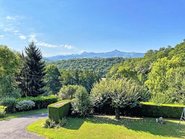 A lush garden with a variety of trees and shrubs, a well-maintained lawn, and a clear view of distant mountains.