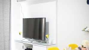 Ett modernt vardagsrum med en platt-TV, ett matbord med gula stolar och en vit luftkonditioneringsenhet på väggen.