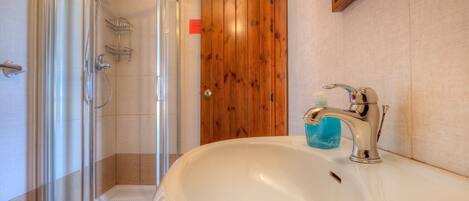 A bathroom with a glass shower enclosure, a wooden door, and a sink with a modern faucet.