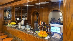 Un espace bar avec des lambris en bois, un présentoir de boissons en bouteille et une enseigne indiquant « GO GREEN GROVE, maison d’hôtes – Malte ».
