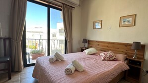 Une chambre d’hôtel avec un grand lit, deux lampes de chevet, une tête de lit en bois et un balcon avec des rideaux.