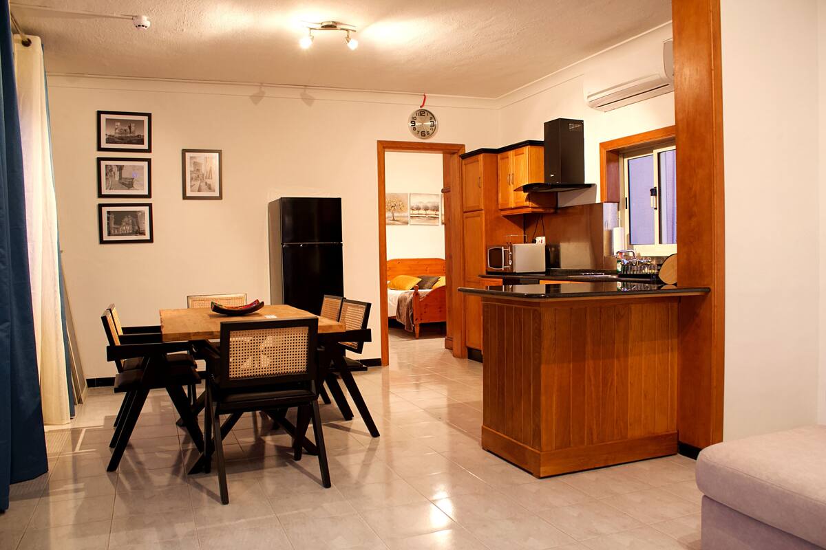 A compact kitchen with a dining area, wooden cabinets, a refrigerator, and a microwave.