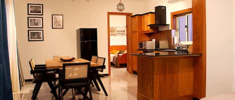 A compact kitchen with a dining area, wooden cabinets, a refrigerator, and a microwave.