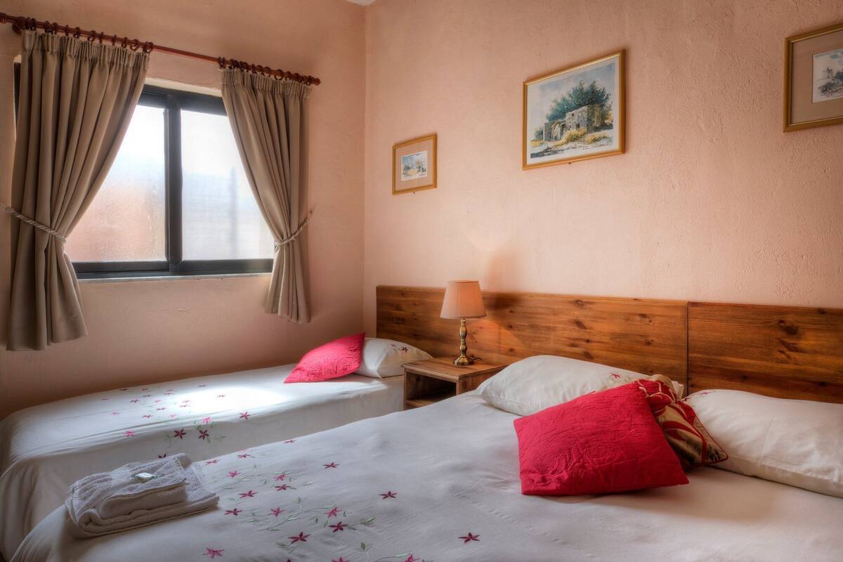A hotel room with two beds, a wooden headboard, a window with curtains, and a lamp on a nightstand.