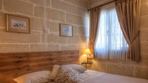 Une chambre à coucher avec une tête de lit en bois, deux tableaux encadrés au mur, une lampe de chevet et une fenêtre avec des rideaux.