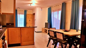 Une cuisine avec des meubles de rangement en bois, une table à manger avec des chaises et un téléviseur.