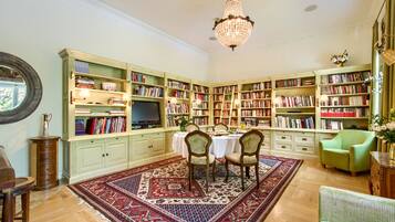 Una biblioteca con estanterías, un candelabro, un comedor con sillas y un sillón verde.
