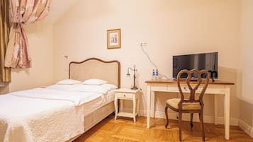 Een slaapkamer met een bed, een bureau met stoel, een televisiescherm en een kroonluchter.