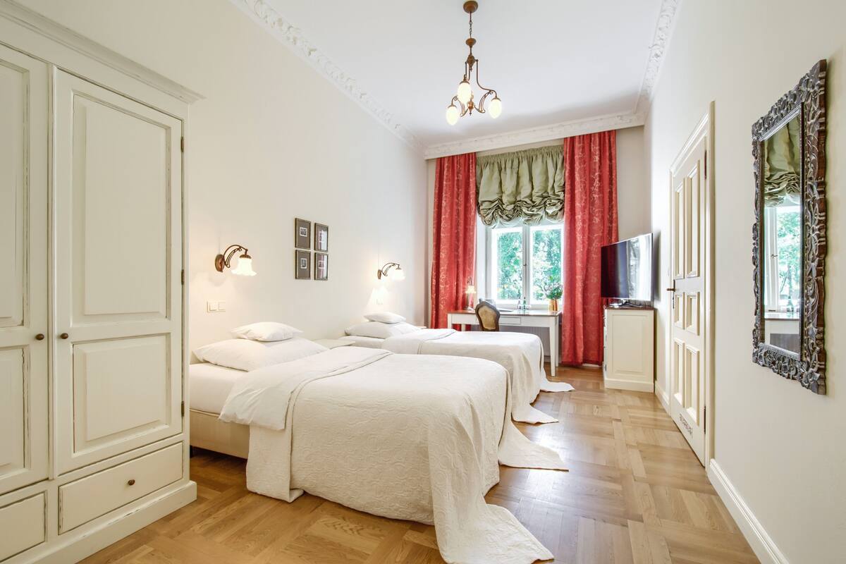 A hotel room with two beds, a desk, a TV, and a large mirror.