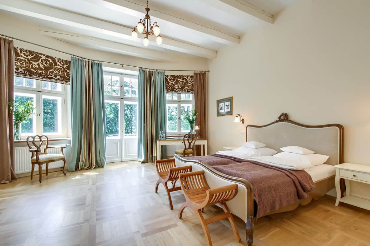 A bedroom with a large bed, wooden chairs, a desk, and a window with curtains.