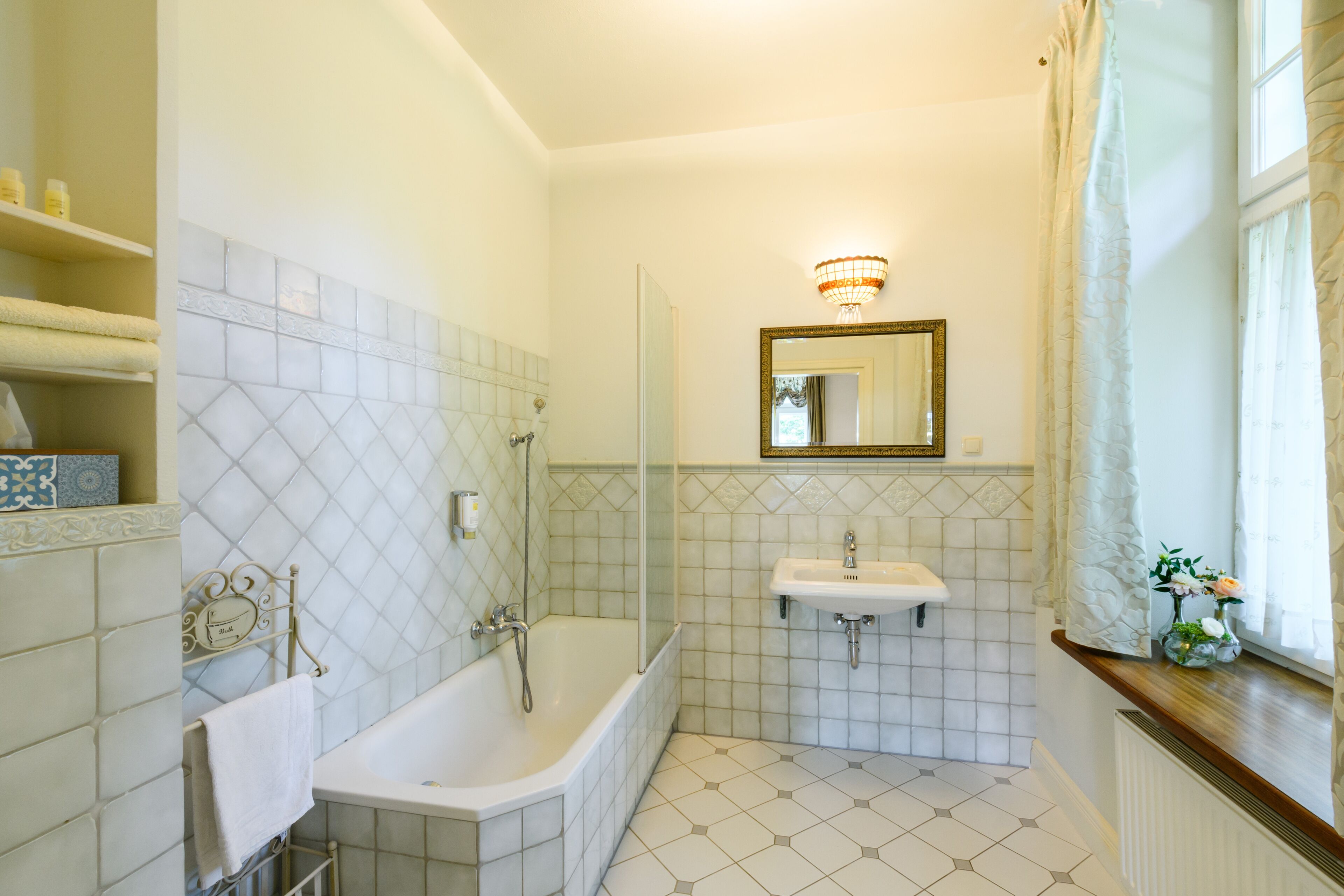 Un baño con bañera, lavabo, espejo y ventana con cortinas.