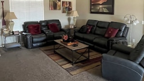 A living room with a sectional sofa, a coffee table, a ceiling fan, and a window with blinds.