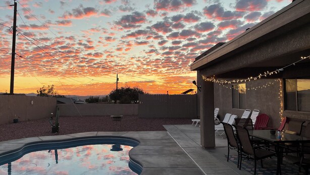A backyard with a swimming pool, outdoor seating, and a sunset view.