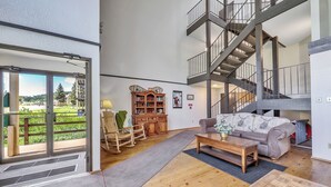 A spacious living area with a wooden floor, a sofa, a rocking chair, a wooden cabinet, and a staircase.