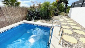 Une piscine dotée d’un bord décoratif, entourée d’un chemin de galets et agrémentée de différentes plantes.