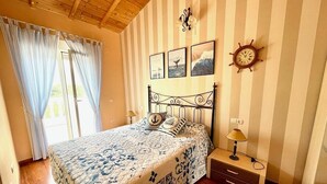 Une chambre avec un mur à rayures, un lit recouvert d’une couvre-lit sur le thème de la marine, une horloge murale et une fenêtre avec des rideaux.
