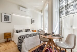 A bedroom with a bed, bedside tables, a round table with chairs, and a large window. - Welcoming Central Studio by PortoDreamStays (Porto)