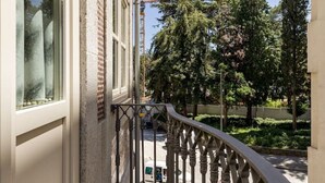 Un balcon étroit avec une rambarde en métal, une vue dégagée sur la rue et des arbres en arrière-plan.