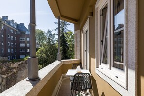 Un balcon avec une table et des chaises, une fenêtre et une vue sur des immeubles et des arbres.